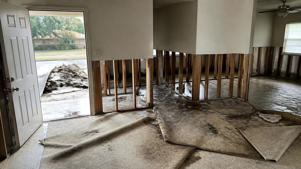 A flood-damaged house gutted with the lower drywall and carpet removed and debris at the curb