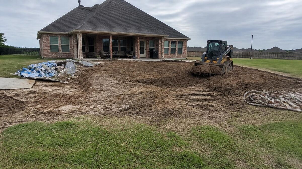 A skid steer spreading fill where an in-ground pool was removed behind a newer brick house